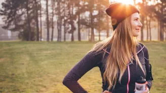 Woman wearing active wear and holding a water bottle in a park during winter.