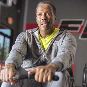 An African American man exercises on a rowing machine at the gym.