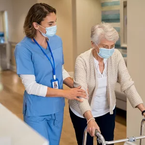 A Nurse Helps an Elderly Patient Navigate the Hallway of the Facility.	