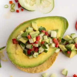 Half an avocado filled with avocado salsa on a white surface