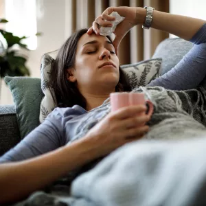 Woman sick with the flu lying on couch with cup of tea.