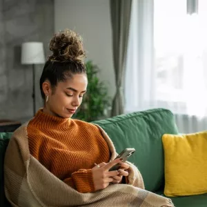 Woman sitting on green couch and looking at her phone.