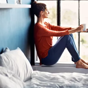 A woman sitting on a windowsill drinking tea.