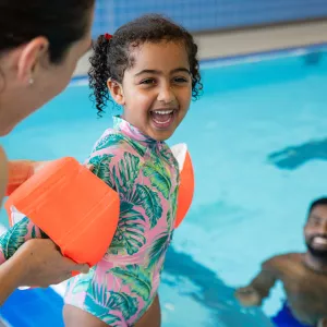 Mom helping child put on arm floats before going into pool.