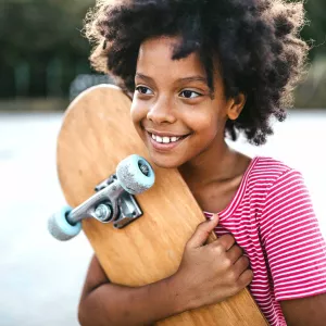 A Kid Squeezes Her Skateboard While Smiling in the Park.