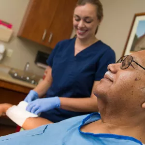 A nurse tends to a Hispanic man's wrist wound.