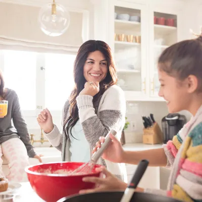 A Caucasian mom dances around the kitchen with her two daughters.