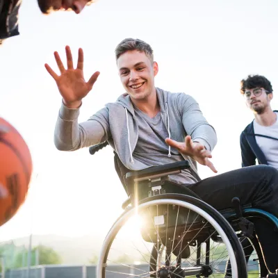 Older teens playing basketball one of which is in a wheelchair 