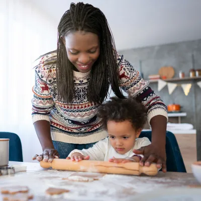 Mom and child baking cookies using rolling pin in the kitchen.