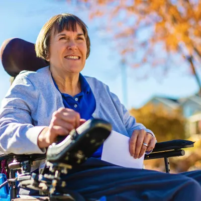 A mature woman in a wheelchair and is outside.