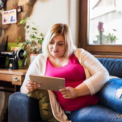 A Woman Lays on Her Couch Reading a Tablet with a Smile on Her Face.