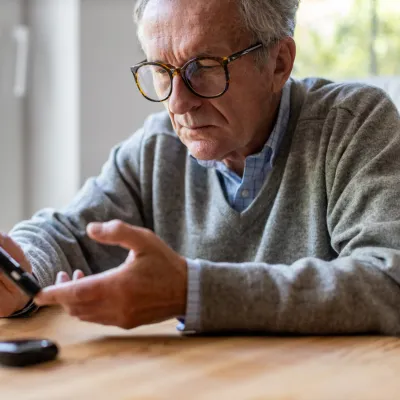 A Senior Checks His Glucose Levels with a Device While Sitting at the Kitchen Table