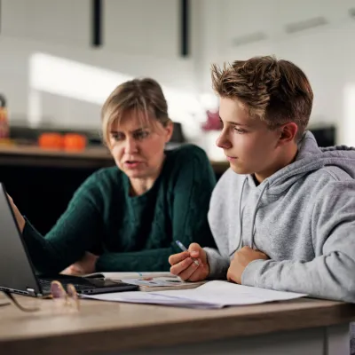 A Mother and Son Work on School Work with a Laptop on the Kitchen Table