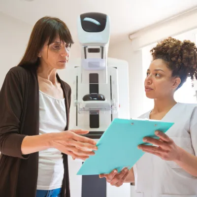 A Woman and a Provider Go Over a Chart in Front of Mammogram Machine