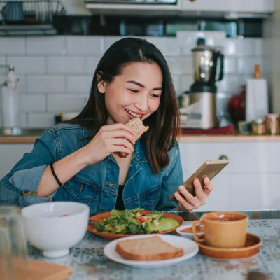 A Woman Smile at Her Mobile Device as She Eats a Balanced Breakfast