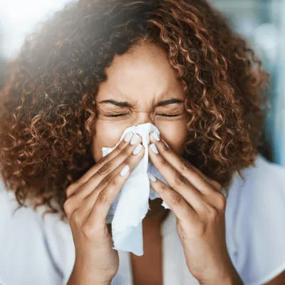A Woman Sneezes into a Tissue at Home