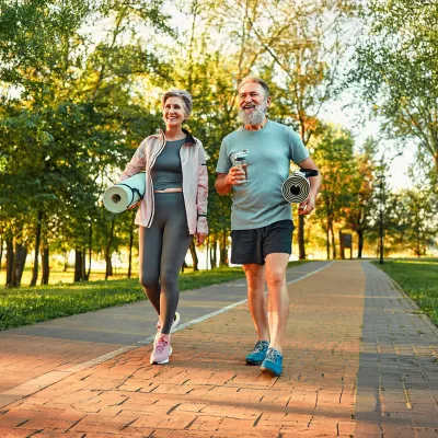 Senior Man and Woman Walking with Yoga Mats in Park