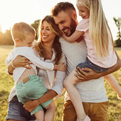 A family of four, the mother holding the son and the father holding the daughter, all laughing and smiling. The sun setting behind them.