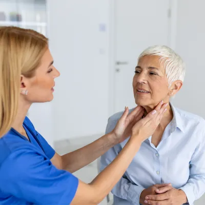 Doctor feeling the neck of a woman to check her thyroid.