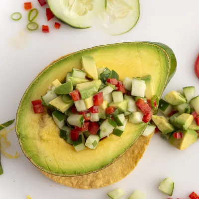 Half an avocado filled with avocado salsa on a white surface