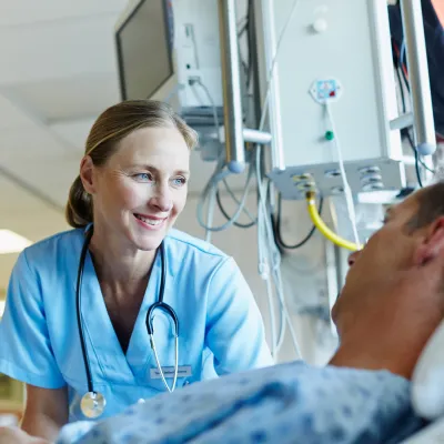 A smiling female physician reassures her male patient in a hospital room.
