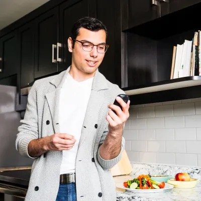 A Man Wearing Glasses Checks His Glucose Levels Before Eating a Healthy Meal in His Kitchen