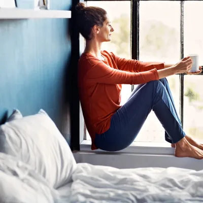 A woman sitting on a windowsill drinking tea.