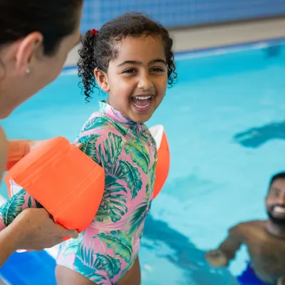Mom helping child put on arm floats before going into pool.