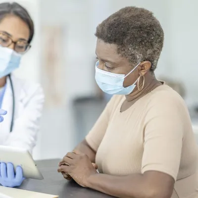 Doctor talking with patient about results on tablet, wearing masks