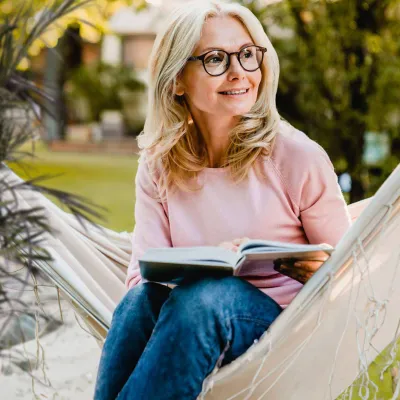 Woman sitting in hammock reading a book.
