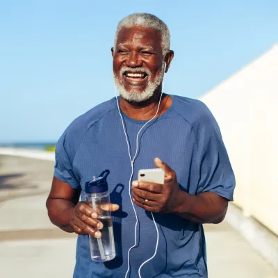 Older man running outdoors listening to music on phone.
