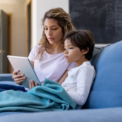 A mother and son sitting on a couch and using a tablet.