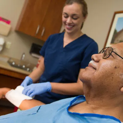 A nurse tends to a Hispanic man's wrist wound.