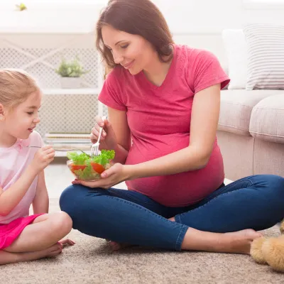 Pregnant mother with daughter eating salad.