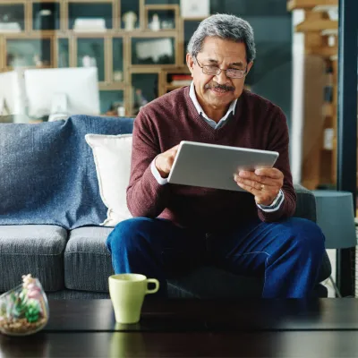 Senior man checking iPad while sitting on a couch while at home.