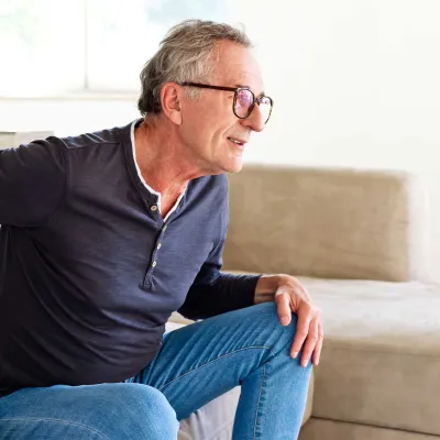 A senior gentleman showing discomfort while getting up from his couch
