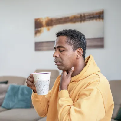 A man with a sore throat sips a cup of hot tea.