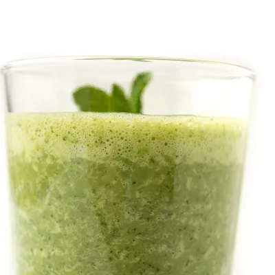 Clear glass of green smoothie with sprig on top.