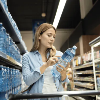 Woman looking at a water bottle at a grocery store.