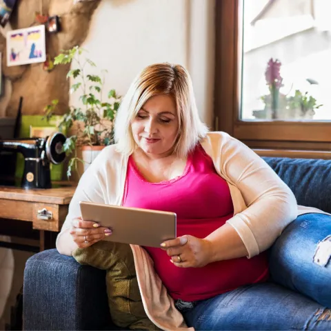 A Woman Lays on Her Couch Reading a Tablet with a Smile on Her Face.