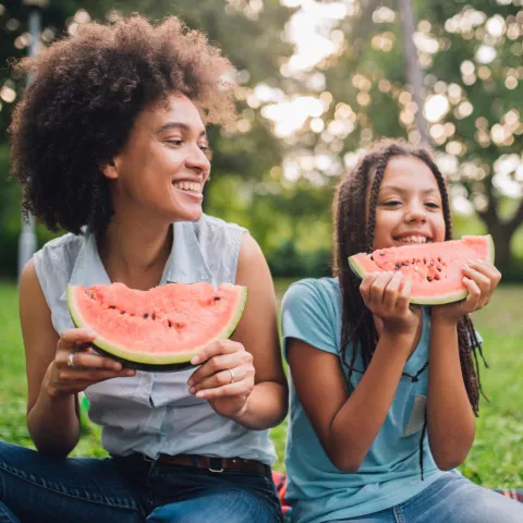 A Mother and Daughter Sit at a Picnic Enjoying Fruit