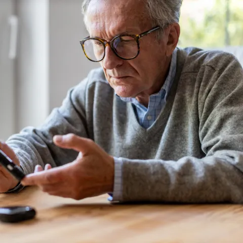 A Senior Checks His Glucose Levels with a Device While Sitting at the Kitchen Table