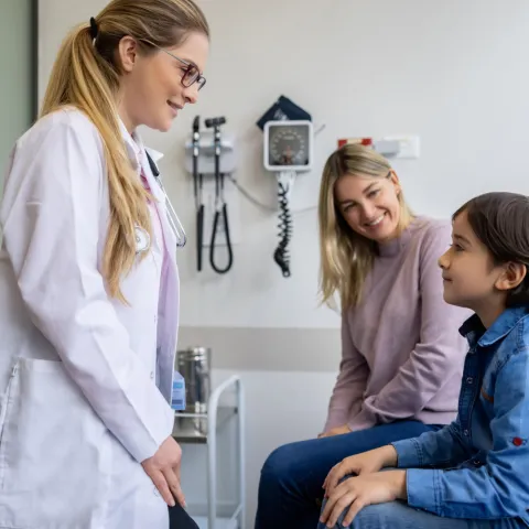 A Mother and Son sit on an Exam Table While They Speak to a Physician