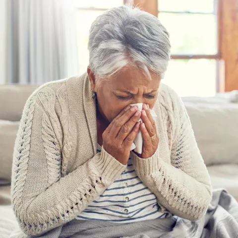 A Senior Woman Blows Her Nose from Seasonal Allergies.