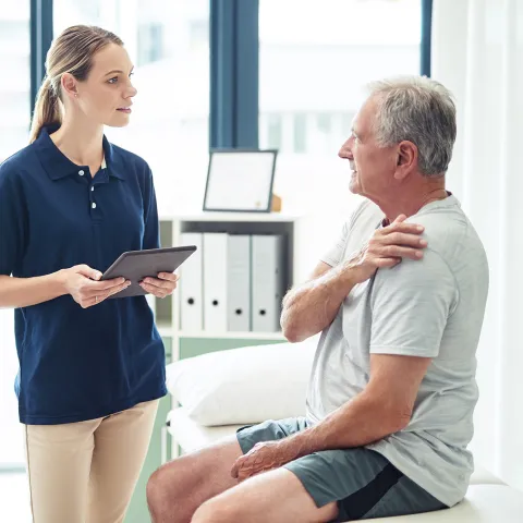 Man holding shoulder talking to woman holding tablet in office.