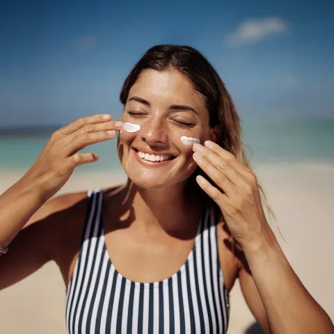 Women applying sunscreen on face at the beach.