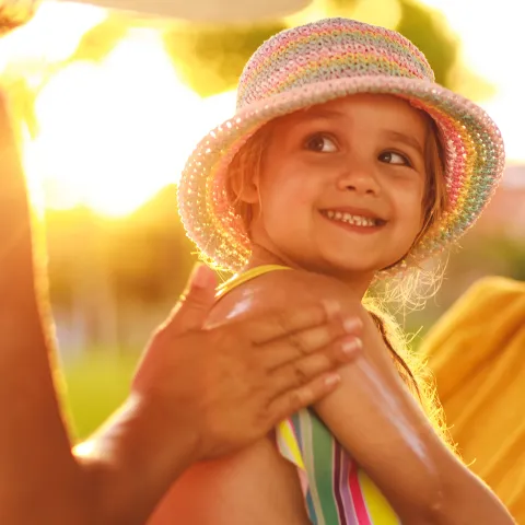 Mother supplying sunscreen to child outdoors.