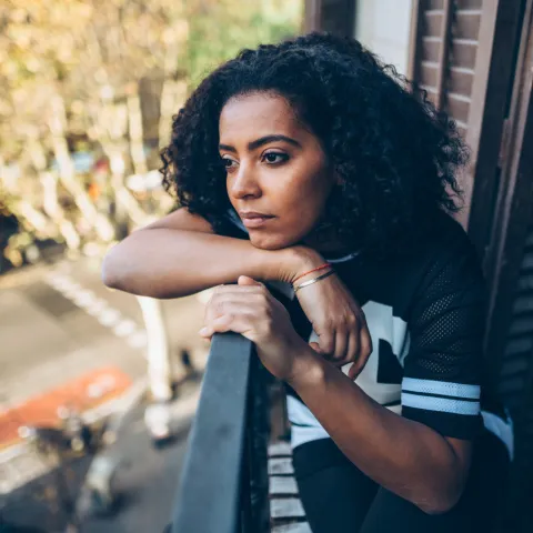A Woman With a Concerned Look on Her Face Stares at Street From Her Balcony.