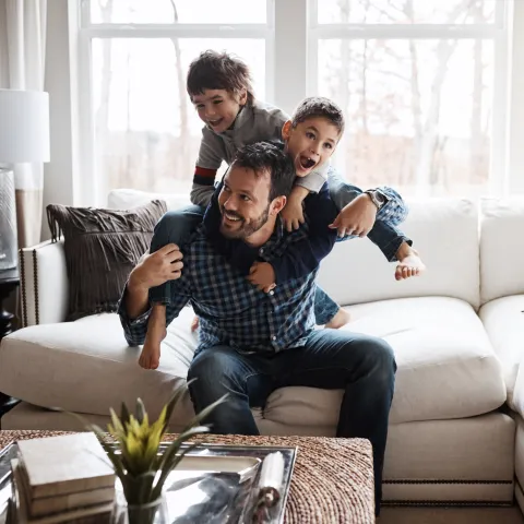 A father and his two sons playing on the sofa of their living room.