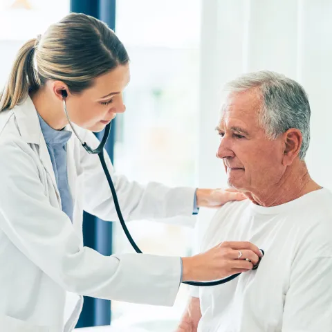 Doctor checking an older male patient's lungs with a stethoscope.